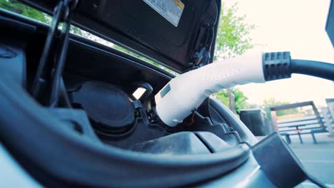 refueling process of an electric car. a shot under the hatch where the electric eco car charges. the electric car charging hatch opens automatically. a male hand inserts an erectile car