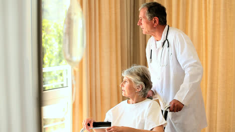 médico y paciente en silla de ruedas mirando por la ventana
