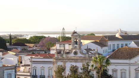 Kreisen-Um-Den-Alten-Kirchturm,-Freigelegter-Glockenturm,-Umgeben-Von-Traditionellen-Alten-Europäischen-Gebäuden-In-Faro,-Portugal,-Luftaufnahme