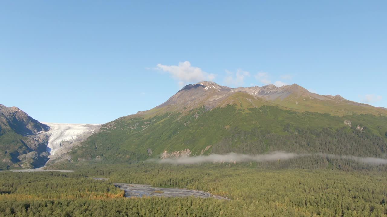 A slowly horizontal moving aerial view of Exit Glacier in Kenai Fjords National Park during fall, featuring a river, the majestic mountains, and the glacier itself. Captured near Seward, Alaska