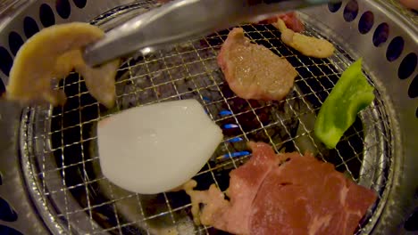 two tongs flipping raw meat and vegetables on yakiniku japanese bbq