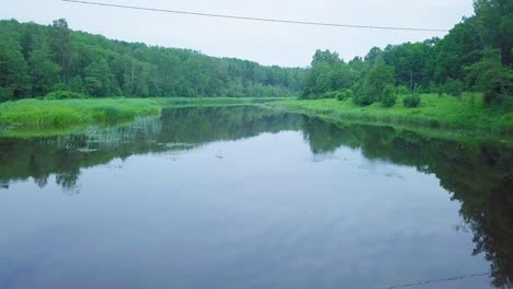 Aerial-view-of-a-Venta-river-on-a-sunny-summer-day,-lush-green-trees-and-meadows,-beautiful-rural-landscape,-wide-angle-drone-shot-moving-forward-low-over-the-calm-river