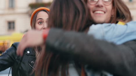 un joven grupo caucásico de amigos en la calle con un smartphone en las manos, luego su amiga se acerca y los abraza