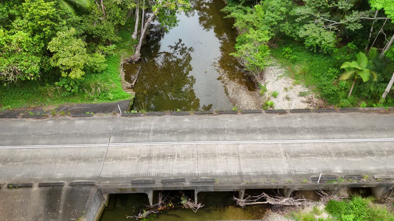 Aerial view of a yellow car driving across a bridge over a river in a vibrant rainforest setting