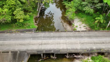aerial view of a yellow car driving across a bridge over a river in a vibrant rainforest setting