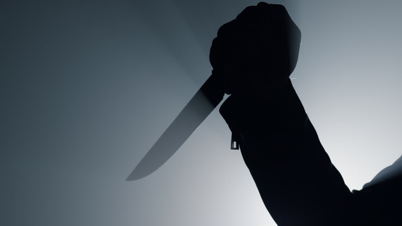 Silhouette man arm holding knife in dark. Criminal hand attacking with dagger.
