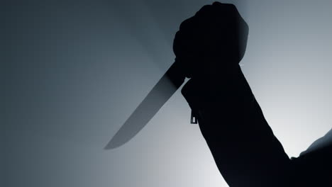 silhouette man arm holding knife in dark. criminal hand attacking with dagger.