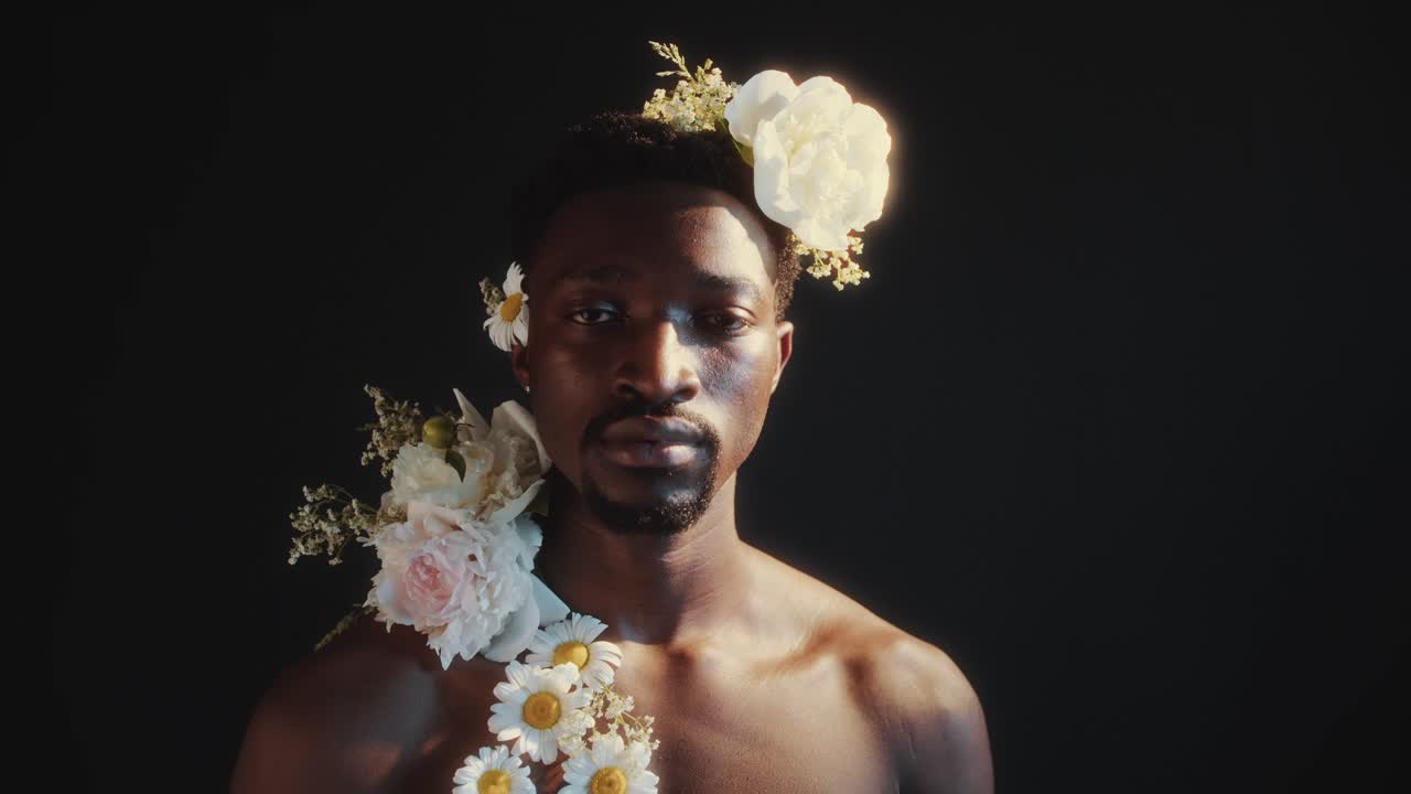 Ritratto di un bell'uomo di colore con fiori sulla testa e sulla spalla.
