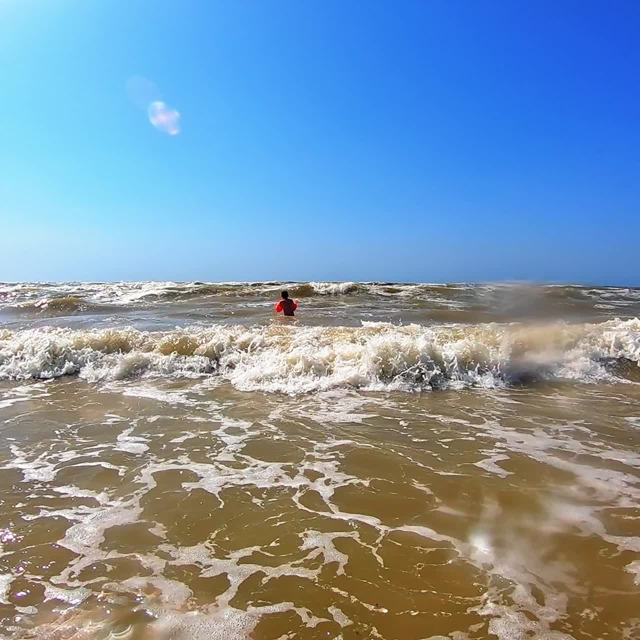 White foam on the dirty sea water. Big waves breaking on the shore. Happy child is having fun in the sea in summer.
