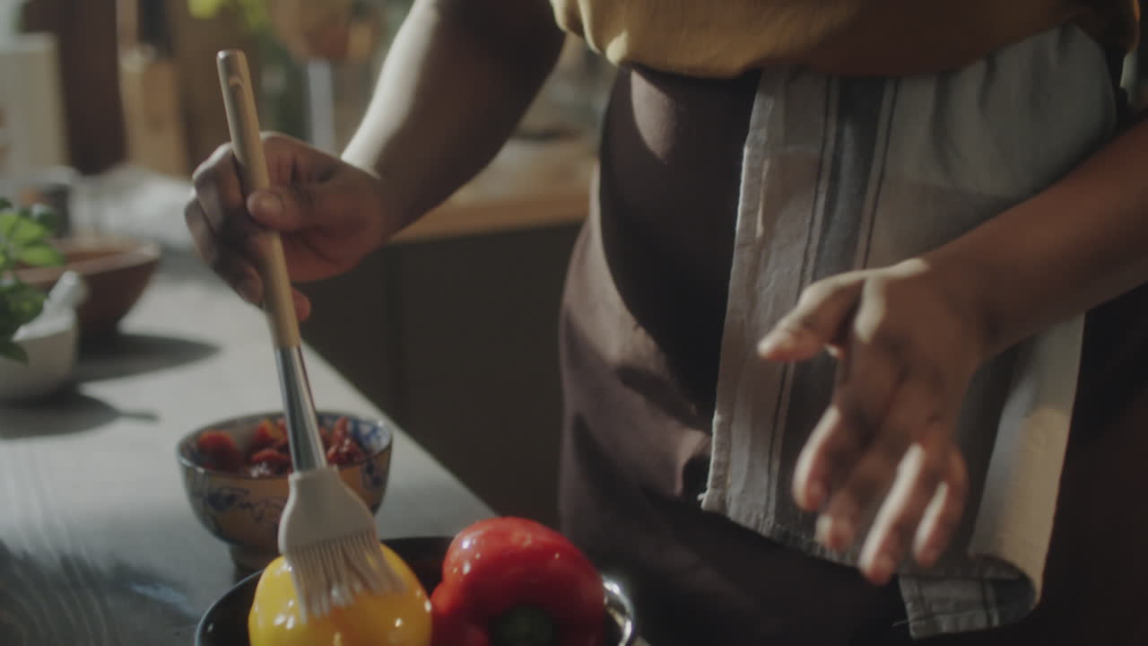 A person preparing food in a kitchen, including stirring ingredients and brushing oil on bell peppers
