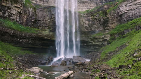 green grass and cascading water falling on black rocks misty, low aerial push in