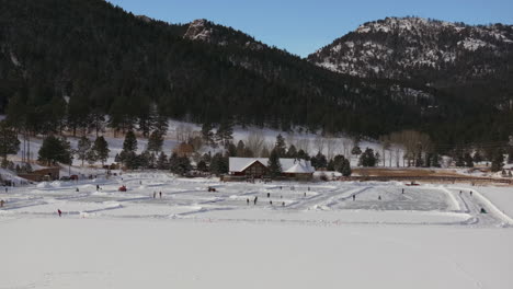 Patinaje-Sobre-Hielo-Patinar-Pista-De-Hockey-Lago-Estanque-Hockey-Invierno-Etown-Casa-Del-Lago-De-Hoja-Perenne-Denver-Campo-De-Golf-Colorado-Aéreo-Cinematográfico-Dron-Soleado-Cielo-Azul-Mañana-Invierno-Fresco-Nieve-Lentamente-Panorámica-Hacia-Arriba-Revelar-Adelante