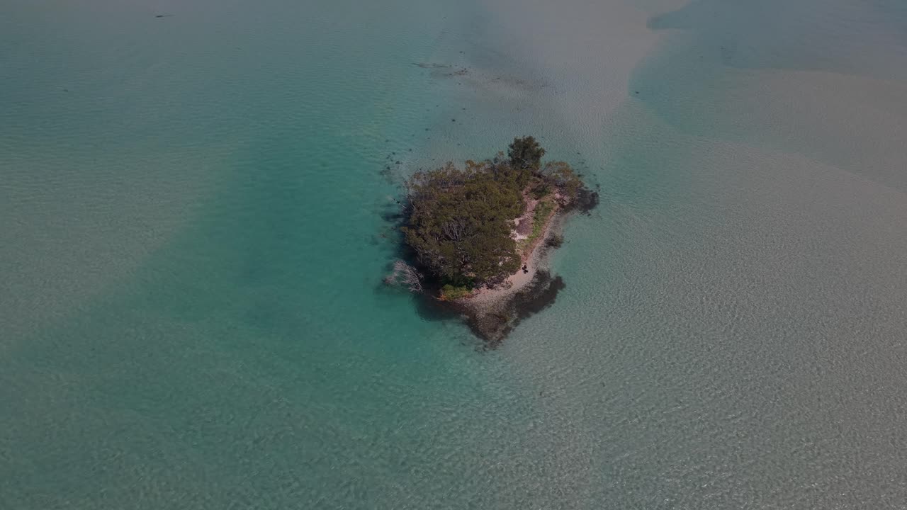 Aerial high angle orbit of pristine waters by island coast, vibrant reef tones and gentle surface texture