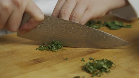 chef slices mint leaves with kitchen knife on wooden cut board