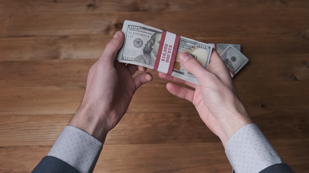 una pila de billetes de 10.000 dólares estadounidenses en manos masculinas sobre un fondo de madera.