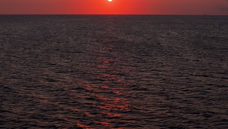 La-Inclinación-Del-Retroceso-Aéreo-Hacia-Arriba-Revela-Una-Hermosa-Puesta-De-Sol-Naranja-Rojo-Fuego-Sobre-El-Agua-Tranquila-Y-Serena-Del-Océano