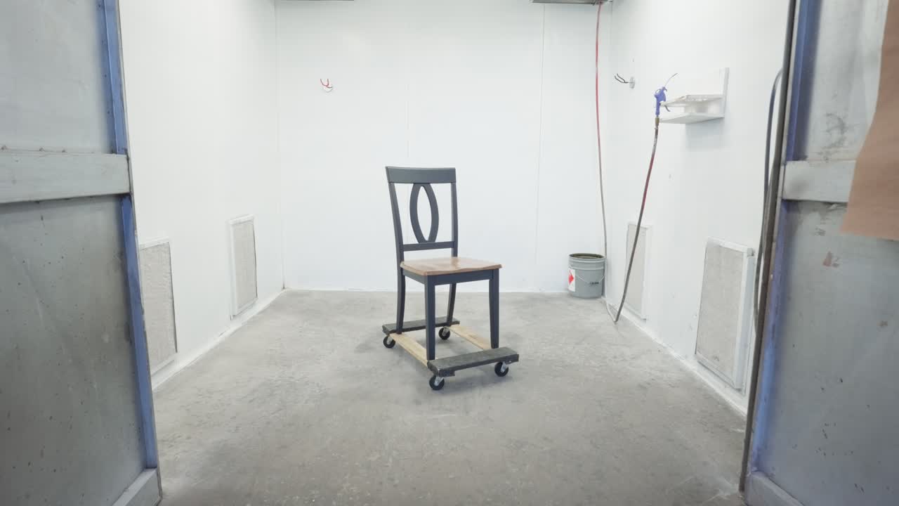 Slow-motion dolly in reveals wooden dining chair on dolly inside paint booth