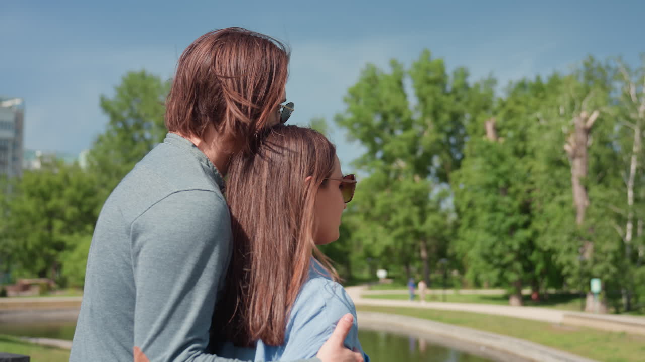 Una pareja comparte un momento tierno cerca del agua, escena tranquila de dos enamorados junto a un lago, pareja serena abrazándose junto a aguas tranquilas en un parque, pareja abrazándose con cariño junto a un lago sereno en un entorno de parque tranquilo