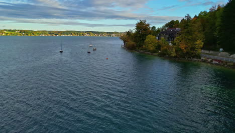 Attersee-Lake-with-sailboats,-autumnal-trees,-and-lakeside-houses-at-dusk-Aerial-shot