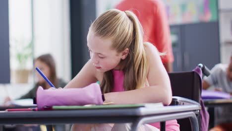 Portrait-of-happy-diverse-schoolchildren-at-desks-writing-in-school-classroom