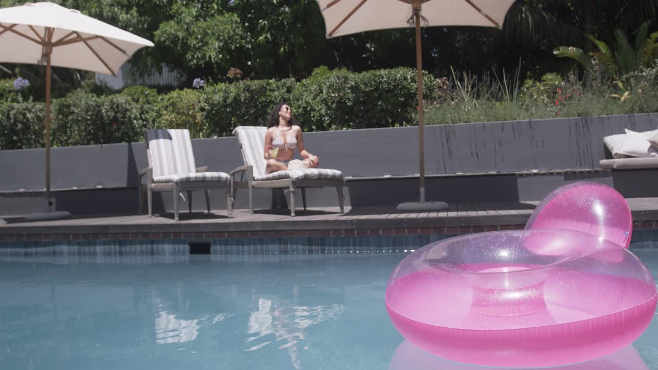 African American woman in bikini at pool adjusting sunglasses tilting back from glare by pink float