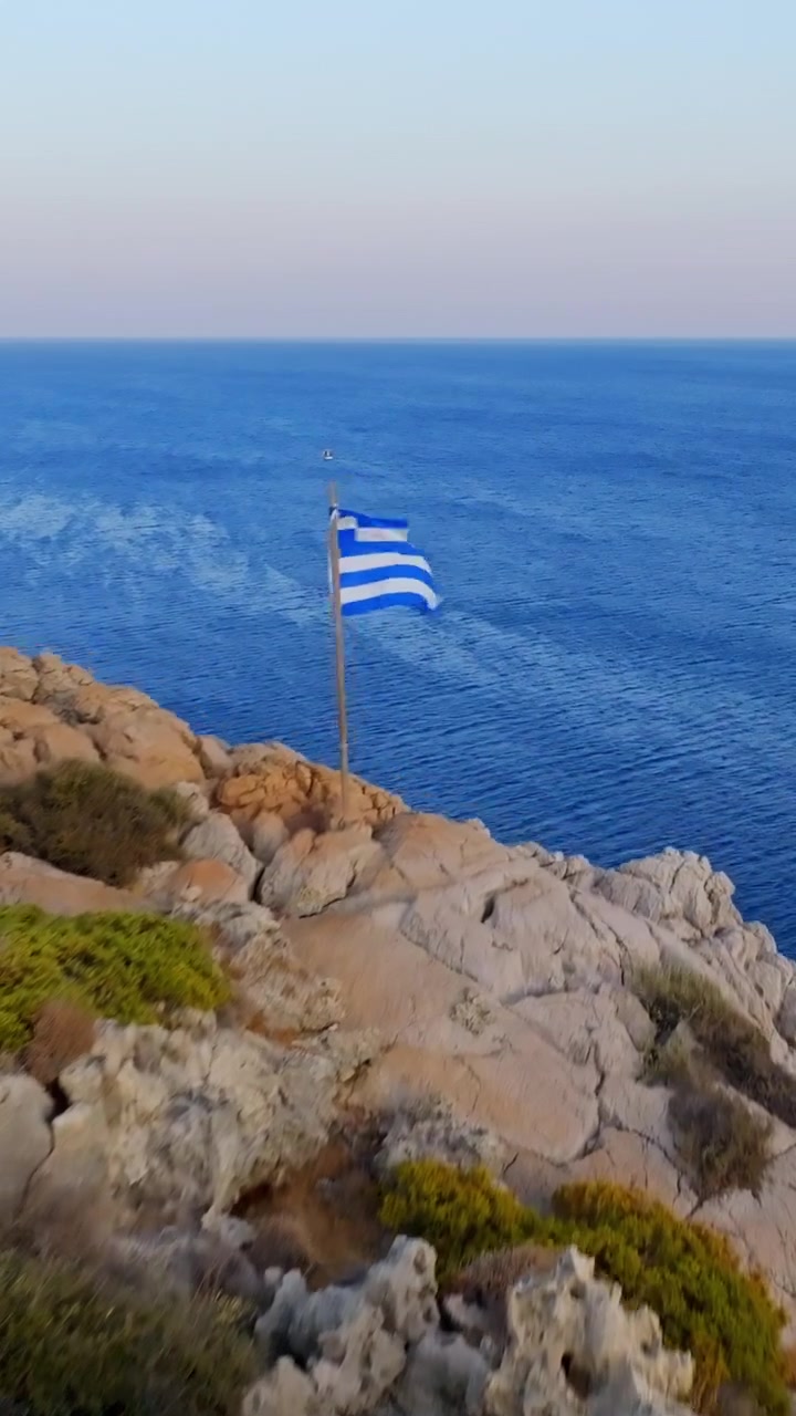 Vertikalt droneoverflyvning av Rhodos' klipper med Hellas' nasjonalflagg