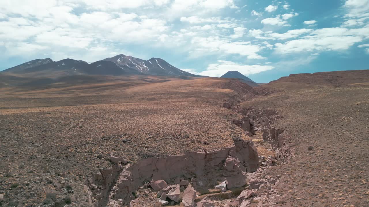 drone volando sobre el borde de un gran cañón en el desierto chileno con un volcán en el fondo