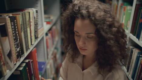 young female student picking up book from shelf in library