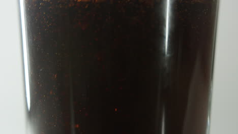 middle section of a clear glass shown being filled with cola drink against clear light background