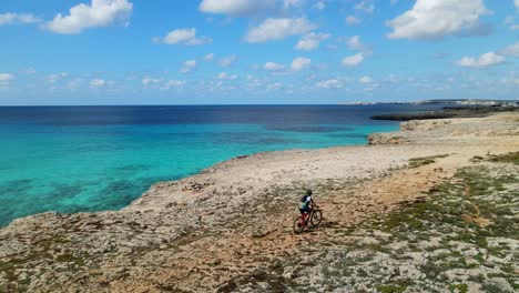 Close-up-drone-panning-around-mountain-bike-rider-mid-race-along-the-coastline-of-Spain