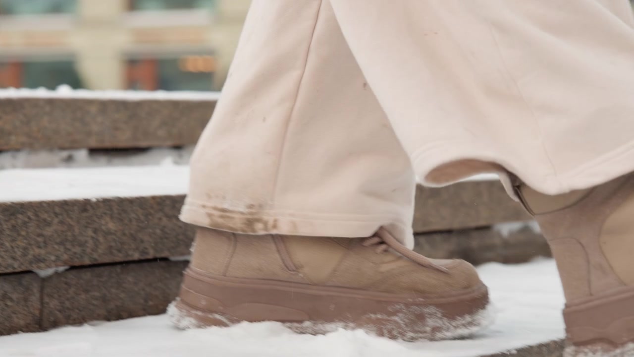 Close low-angle view of lower legs and casual leather or suede boots walking across snow-covered concrete steps and ledges