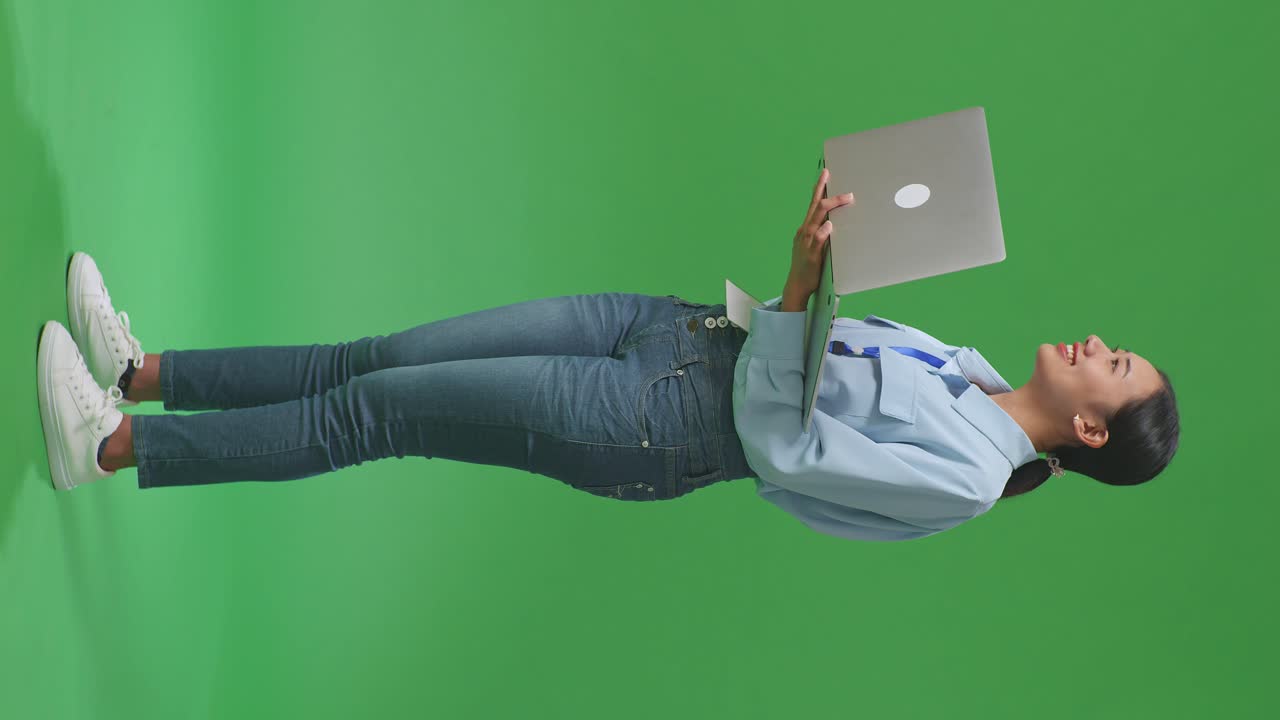 vista lateral de cuerpo completo mujer de negocios asiática usando computadora portátil un mirando a su alrededor en el fondo de la pantalla verde en el estudio