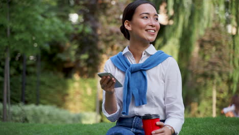 woman reading messages on her phone and drinking a coffee outdoors