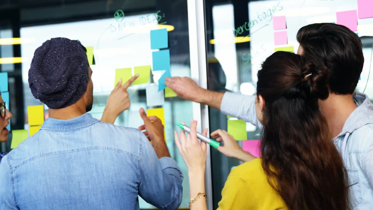 Executives discussing over sticky notes on glass wall