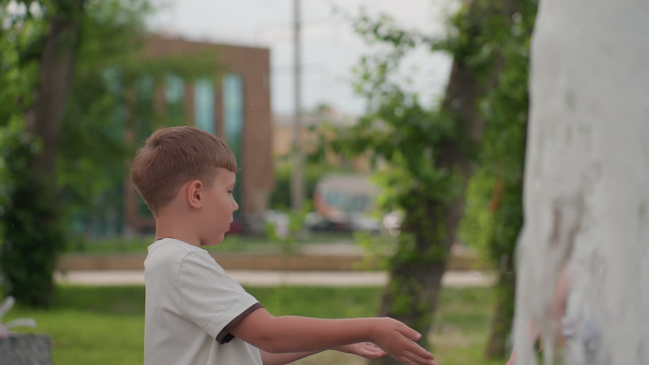 Playful kids chatting and splashing around recreational park fountain, girl with face paint smiling as boy touches water jet, blurred greenery and benches framing summer scene of youthful curiosity