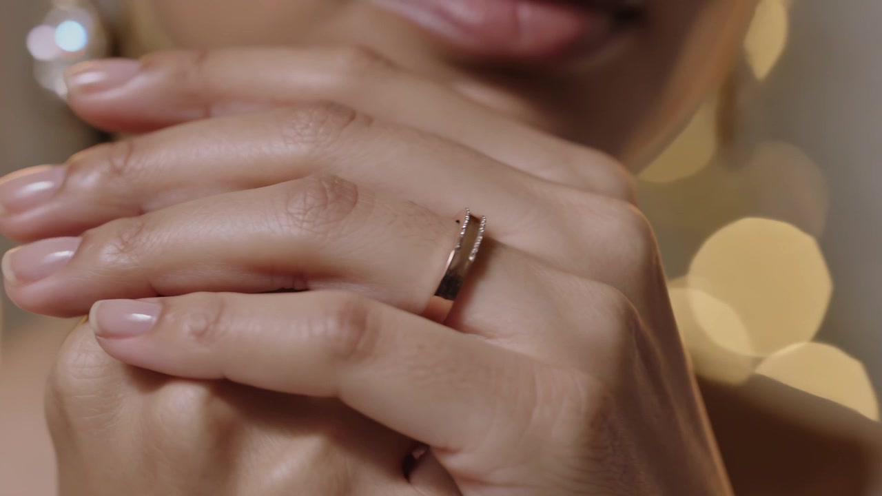 Primo piano iniziale che ritrae una donna che tiene le mani vicino alla bocca in studio, mostrando un anello d'oro e un orecchino.