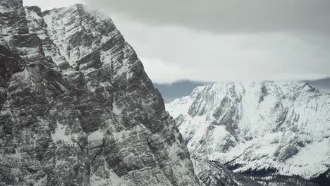 Schwere-Wolken-Hängen-über-Dunklen,-Hoch-Aufragenden-Bergen,-Die-Mit-Einer-Dünnen-Schneeschicht-Bedeckt-Sind