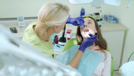 higienista dental que examina los dientes del paciente con un espejo bucal y una sonda dental