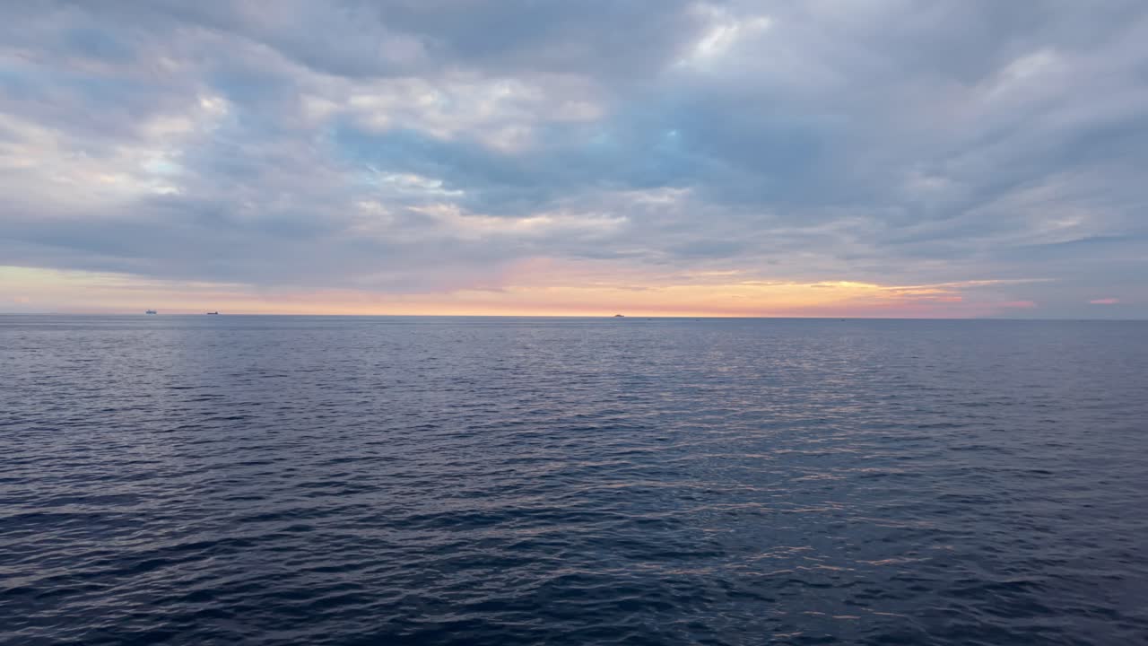 A calm ocean at dawn under a cloudy sky with soft light on the horizon