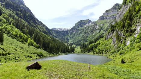 a woman hikes near a serene mountain lake surrounded by lush green valleys on a sunny day