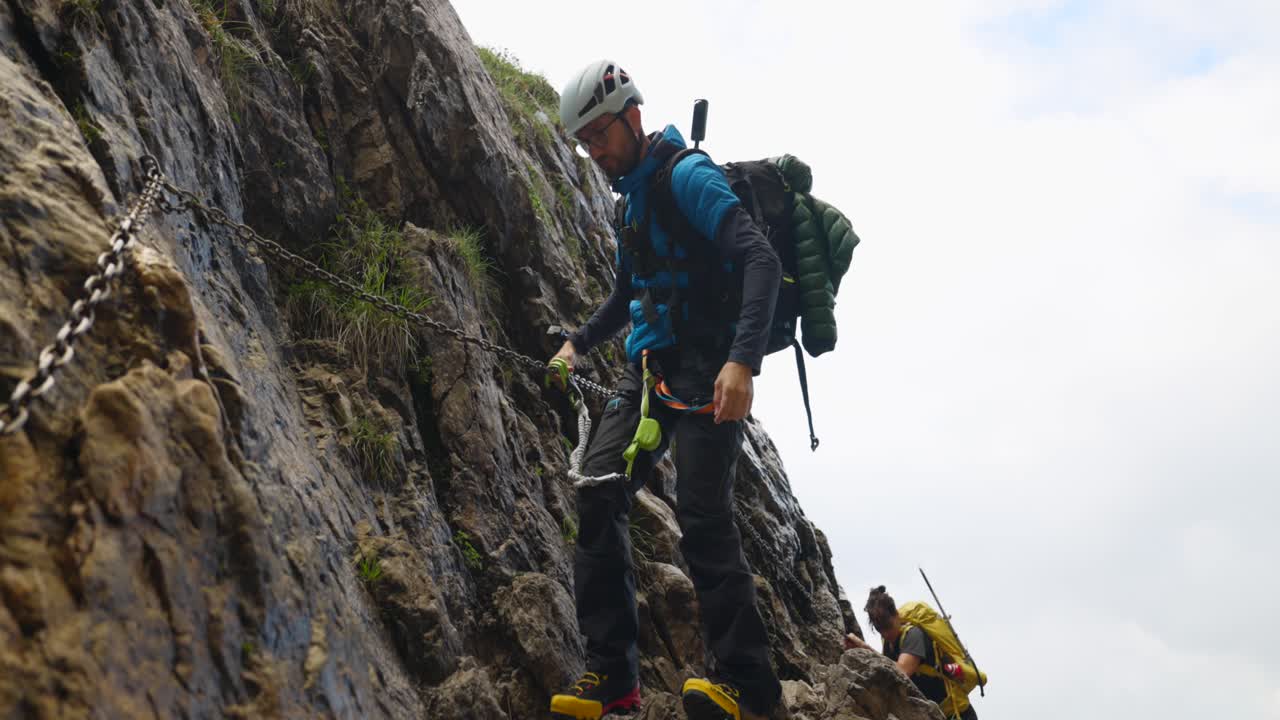 Two Mountain Climbers Gripping Metal Chains as They Navigate the Steep Cliffs of Mount Grignetta in Lombardy, Italy - Handheld Shot