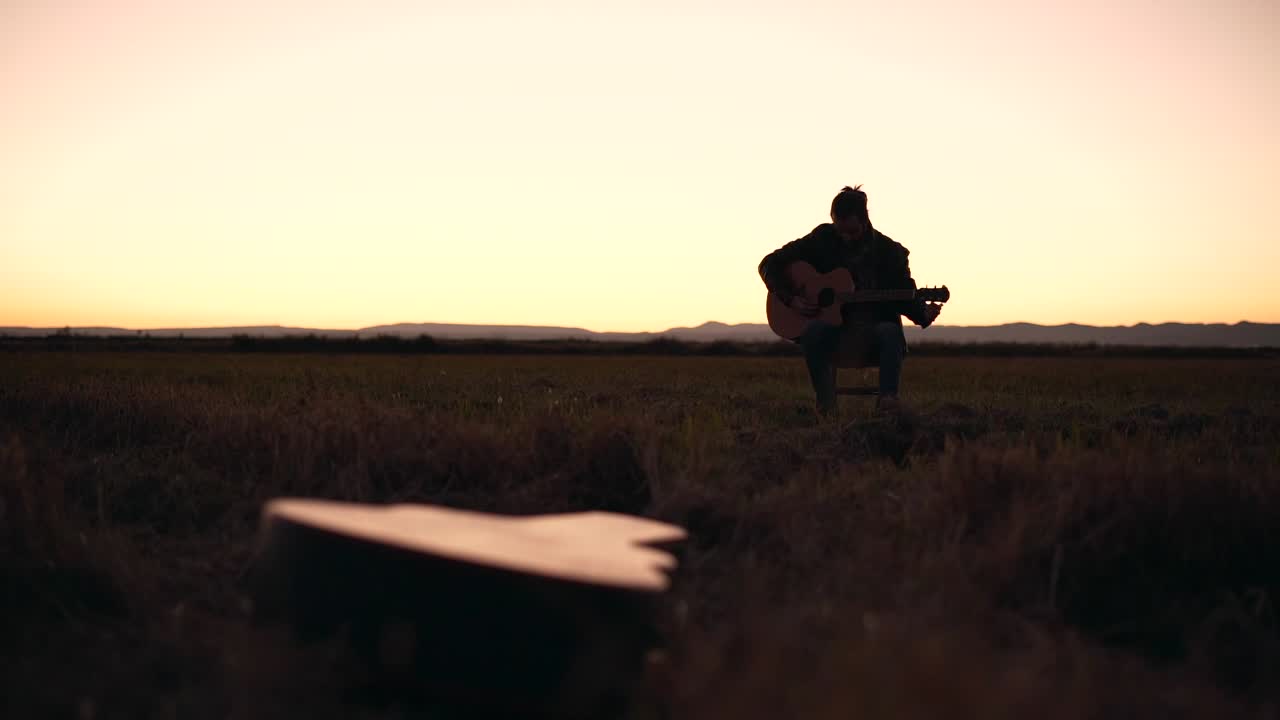 Silhouette di un musicista che suona la chitarra al tramonto