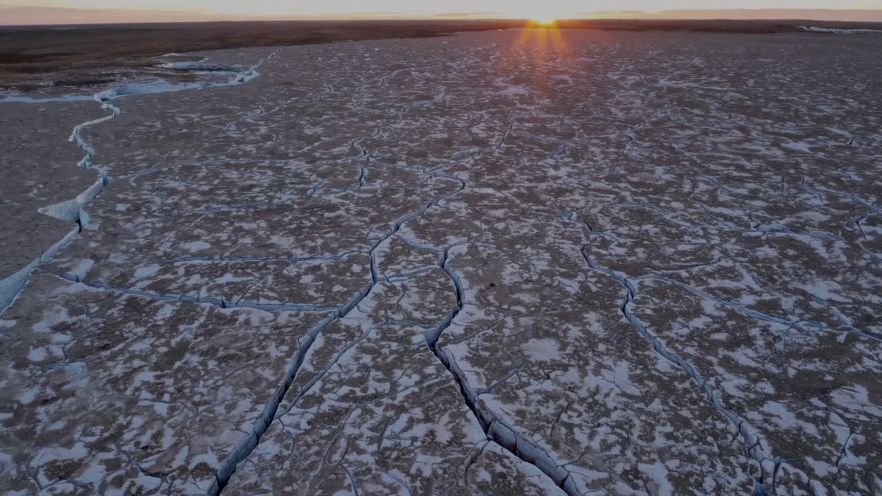 Aerial view of cracked ice sheets in a vast frozen landscape at sunset, showcasing a dramatic