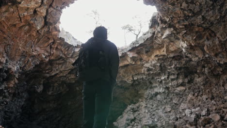 hiker admires large skylight in cave roof at el malpais national monument