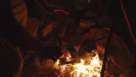 caucasian male survivalist warming hands in evening campfire at camp in wilderness