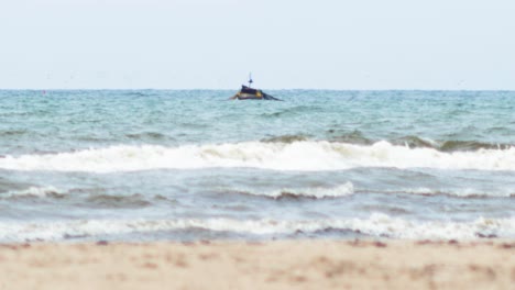 small wooden coastal fishing boat cast their nets in baltic sea near the liepaja , overcast day, heat waves, white sand in foreground, low angle medium distant shot