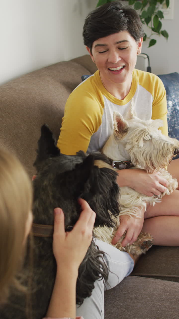 행복한 백인 레즈비언 커플이 집에서 개와 포옹하는 수직 비디오