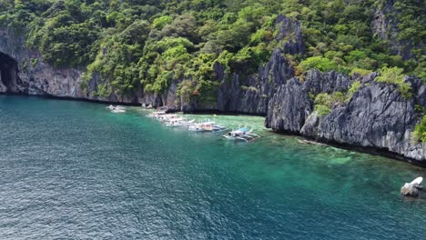 Aerial,-Outrigger-Island-hopping-Tour-Boats-anchored-at-Hidden-Beach,-El-Nido---Philippines-in-a-tropical-Scenery-of-lush-leafy-Karst-cliffs-and-crystal-clear-water