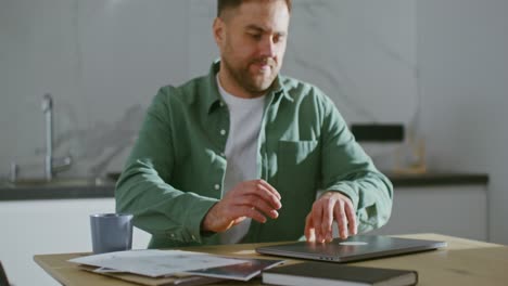 hombre trabajando en una computadora portátil en la cocina de su casa