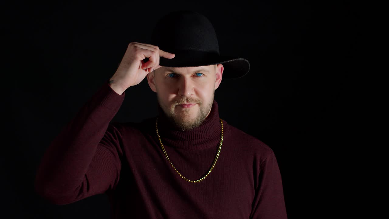 검은 모자와 금 사슬을 입은 남자가 포즈를 취하고 있다